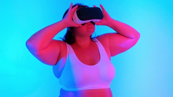 身穿运动服的超重女性和戴Vr耳机的女性在蓝色背景和红色照明的工作室里摆姿势 — 图库视频影像