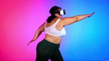 Aşırı kilolu eşofmanlı ve VR kulaklıklı bir kadın mavi ve kırmızı arka planı olan bir stüdyoda egzersiz yapıyor.