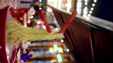 Çin yemek çubuklarının Çin Mahallesi 'nde akşam vakti Londra' da erişte satışı dikey olarak görülüyor. Dekorasyonlu, aydınlatmalı ve arka planda insanları hareket ettiren yaya caddesi