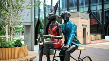 Londra, İngiltere 'de, Canary Wharf bölgesinde bisiklete binmiş tavşan ve köpek kafası olan iki kişinin sanat galerisi.