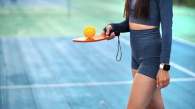 Dış sahada Pickleball oynadığı için bir raketi dengeleyen takım elbiseli bir kadının yakın görüntüsü. Yavaş çekim