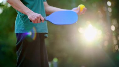 Pickleball oynayan bir adam, dışarıda bir sahada raketle top sahası yapıyor. Yavaş çekim