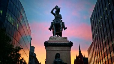 İngiltere, Londra 'da gün batımında Prens Albert Binicilik Heykeli. Çevresindeki modern binalar, arka plandaki günbatımı gökyüzü.