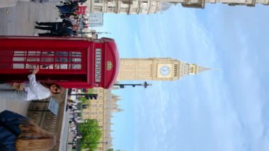 LONDON, UNITED KINGDOM - 13 Eylül 2023: Yürüyen insanlar ve hareket eden arabalarla şehir merkezinin dikey sokak manzarası, Elizabeth Tower 'ın arka planında telefon kulübesi