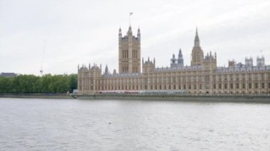 Londra, BİRLİK KINGDOM - 11 Ağustos 2023 'te şehir merkezindeki Westminster Sarayı manzarası. Yürüyen insanlarla dolma sokak, yüzen teknelerle Thames nehri.