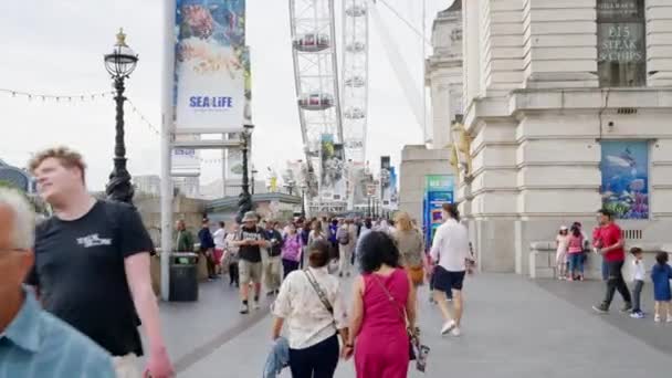 ロンドン United Kingdom August 2023 複数の歩行者とクイーンズウォークからダウンタウンのロンドンアイフェリスホイールの眺め — ストック動画