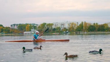 Chisinau, Moldova - 25 Ekim 2023: Gün batımında Valea Morilor gölünde yüzen ördeklerin yanında yüzen bir adam. Yavaş çekim