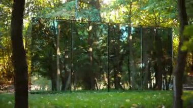 Doğadaki ayna yüzüyle glamping yapan bir cam ev manzarası. Çevrede yemyeşil orman
