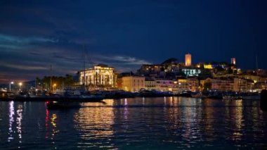 Fransa 'nın Cannes limanının gece vakti demirli ve yüzen yatlarıyla manzarası. Şehir manzarası, uzaktaki bir tepede Castre müzesi, aydınlatma.