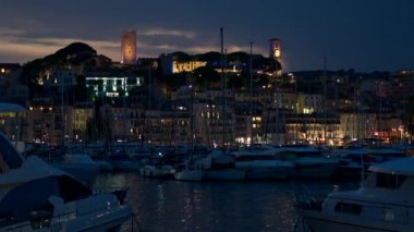 Fransa 'nın Cannes limanının gece vakti çoklu demirlemiş yatlarıyla manzarası. Şehir manzarası, uzaktaki bir tepede Castre müzesi, aydınlanma. Yavaş çekim
