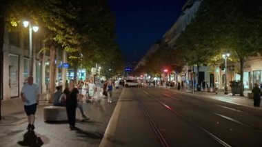 Güzel, Fransa - 25 Eylül 2023: akşam şehrin sokak manzarası. Birden fazla yürüyen insan, dükkanlar ve aydınlatma ve yeşillik olan klasik binalar.
