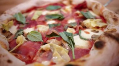 İtalyan restoranındaki capricciosa pizzasının prosciutto, enginar, peynir ve fesleğenli yakın görüntüsü.