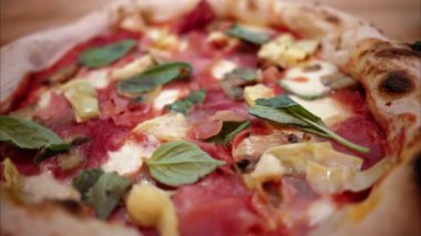 İtalyan restoranındaki capricciosa pizzasının prosciutto, enginar, peynir ve fesleğenli yakın görüntüsü.