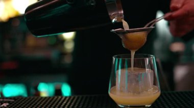 Barmen, karıştırıcıdan büyük bir buz küpüyle bardağa viski kokteyli dolduruyor.