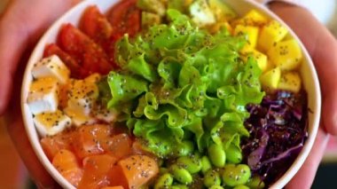 Elinde somon balığı, avokado, feta peyniri, mango, salata ve yeşil edamame fasulyesi olan kadın.