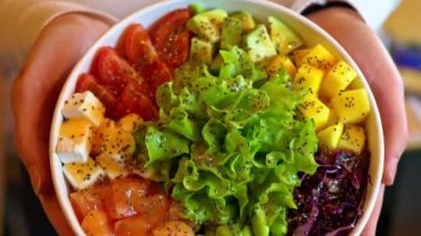 Elinde somon balığı, avokado, feta peyniri, mango, salata ve yeşil edamame fasulyesi olan kadın.