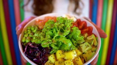 Elinde somon balığı, avokado, feta peyniri, mango, salata ve yeşil edamame fasulyesi olan kadın.
