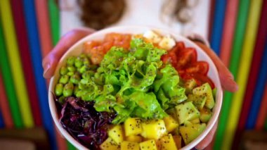 Elinde somon balığı, avokado, feta peyniri, mango, salata ve yeşil edamame fasulyesi olan kadın.