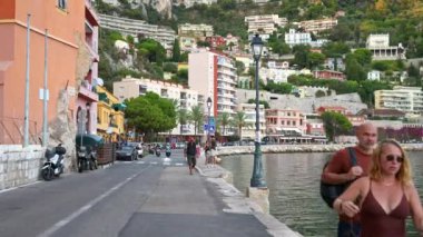 VILLEFRANCHE-SUR-MER, FRANCE - 4 Eylül 2023: Renkli binalar ve restoranlarla çevrili eski liman yakınlarında yürüyen insanlar. Fransız Rivierası 'nda pitoresk bir sahil kasabası.
