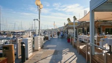 JUAN LES PINS, FRANCE - 4 Eylül 2023: Lüks yatlarla ve yelkenli teknelerle dolu liman yakınlarında yürüyen insanlar