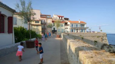 ANTIBES, FRANCE - 5 Eylül 2023: günbatımında Promenade de l 'Amiral-de-Grasse. Akdeniz ve yakınlardaki Lrin adalarının çarpıcı manzarasıyla yürüyen insanlar.
