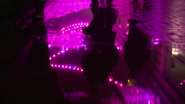 夜间在街上行走的人 在粉色灯光下在地上的雨水中的倒影 — 图库视频影像