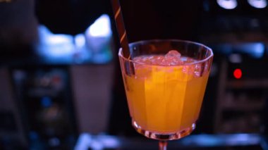 Barmen gece vakti neon ışıkları olan bir barın üzerine buzlu turuncu kırmızı alkol kokteyli döküyor.