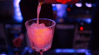 Barmen gece vakti neon ışıkları olan bir barın üzerine buzlu turuncu kırmızı alkol kokteyli döküyor.