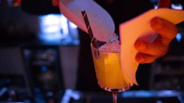 Barmen gece vakti neon ışıkları olan bir barın üzerine buzlu turuncu kırmızı alkol kokteyli döküyor.