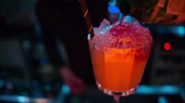 Barmen gece vakti neon ışıkları olan bir barın üzerine buzlu turuncu kırmızı alkol kokteyli döküyor.