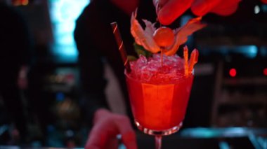 Barmen gece vakti neon ışıkları olan bir barın üzerine buzlu turuncu kırmızı alkol kokteyli döküyor.