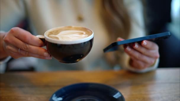 女人一边喝拿铁咖啡一边在智能手机上看内容 — 图库视频影像