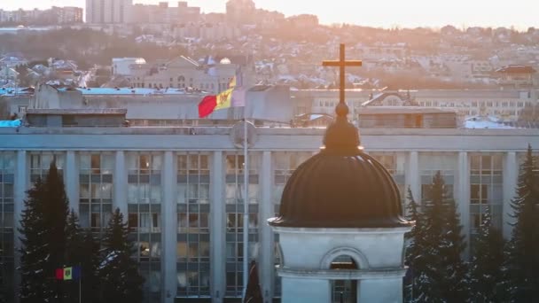 モルドバの国旗と日没時の政府庁舎の空中ドローンビュー ゴールデンクロスは ベルタワーとキリスト降誕のメトロポリタン大聖堂の前景の上にあります スノーウィー シナウ — ストック動画
