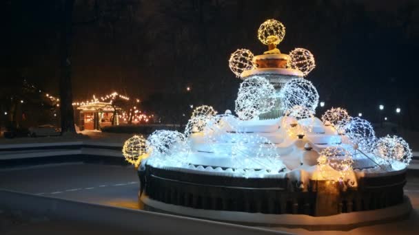 モルドバのシナウ 1月2024 雪の間に中央公園の噴水のクリスマスの装飾 バックグラウンドでコーヒーショップのイルミネーション ウィンターナイト — ストック動画