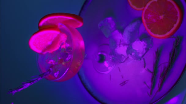 氷とオレンジのスライスで満たされたガラスのカクテル クローズアップ ネオンライト バーティカルショット — ストック動画