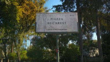 Bükreş meydanının güneş ışığında ağaçlarla çevrili mermer işareti. Roma, İtalya