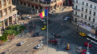 Bükreş, Romanya - 03 Mart 2024: Trafiği hareket ettiren ve gün ışığında yürüyen insanlarla şehir merkezindeki bir kavşağın insansız hava aracı görüntüsü. Ulusal bayrak sallıyor