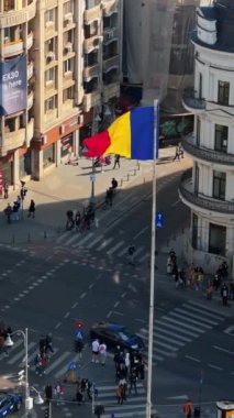 Bükreş, Romanya - 03 Mart 2024: Trafiği hareket ettiren ve gün ışığında yürüyen insanlarla şehir merkezindeki bir kavşağın dikey hava aracı görüntüsü. Ulusal bayrak sallıyor