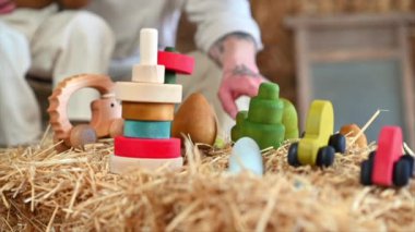 Baba, oğluyla ahır saman balyalarının yanında renkli, ekolojik tahta oyuncaklarla oynuyor.