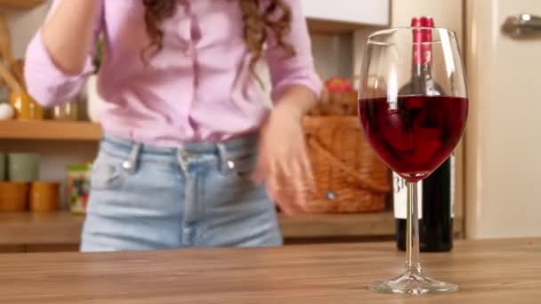 在厨房里跳舞的一个女人面前 桌上放着一只杯子和一瓶红酒 — 图库视频影像