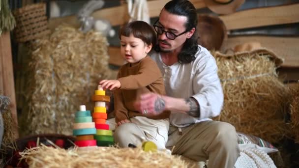 父亲和儿子在谷仓里玩五彩缤纷的生态木制玩具 靠近正方形草包 — 图库视频影像