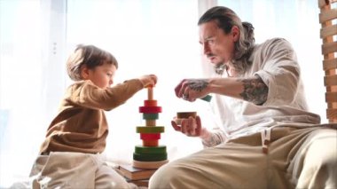 Baba, oğluyla pencerenin yanında renkli, ekolojik tahta oyuncaklarla oynuyor.