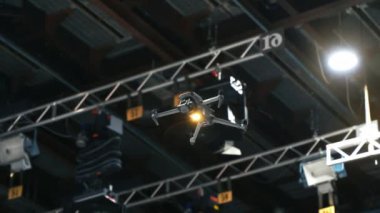 İnsansız hava aracı yanıp sönen stüdyo ışıkları ve kamera ekipmanlarının yanında televizyon setinde uçuyor ve çekim yapıyor.
