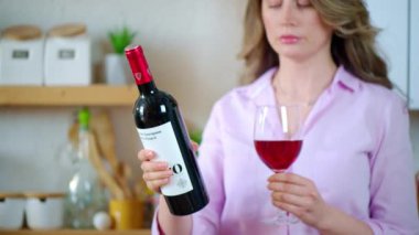 Mutfakta elinde bardak ve bir şişe kırmızı şarap tutan bir kadın.