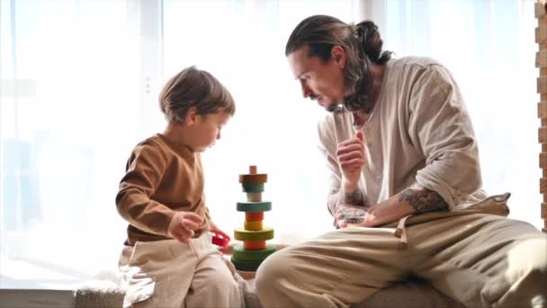 Ojciec Bawiący Się Synem Kolorowymi Ekologicznymi Drewnianymi Zabawkami Przy Oknie — Wideo stockowe