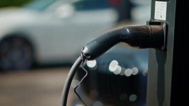 Arka planda beyaz bir araba olan elektrikli araba şarj istasyonuna yakın plan.