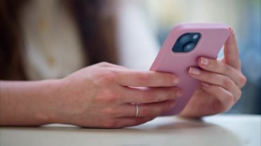 Bir kadın açık bir kafede telefonunu karıştırıyor.