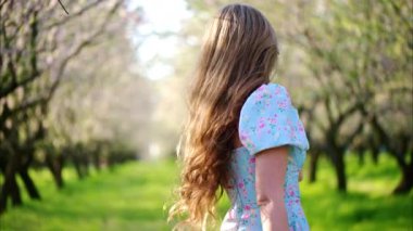 Mavi elbiseli esmer kadın çiçek açan badem ağaçlarının arasında dönüyor.