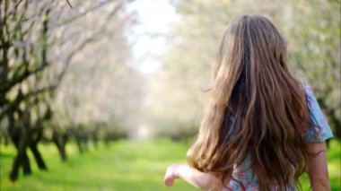 Mavi elbiseli esmer kadın çiçek açan badem ağaçlarının arasında dönüyor.