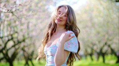 Mavi elbiseli esmer kadın çiçek açan badem ağaçlarının arasında dönüyor.